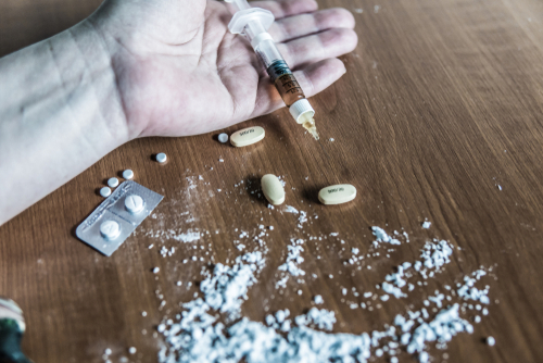 person holding a syringe full of drugs with crushed up pills around them