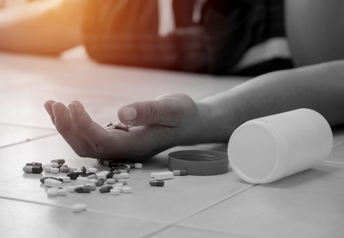 hand laying on grounds next to a spilled bottle of pills