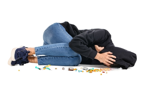 person laying on floor with pills scattered around them 