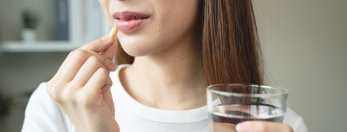 woman putting a pill in her mouth while holding a glass of water