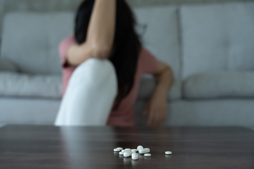 woman sitting with her head down with pills on the table