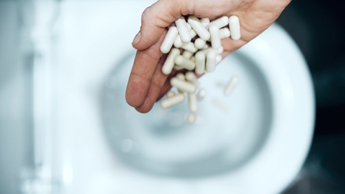 person throwing a handful of pills in the toilet