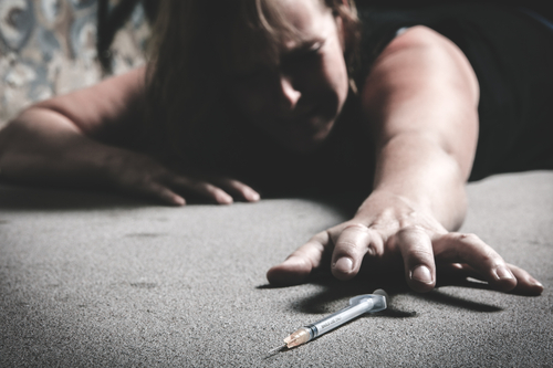 woman laying on ground reaching for heroin needle