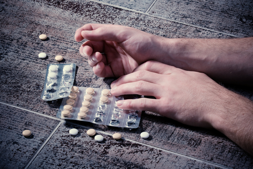 person laying on ground with pills around them